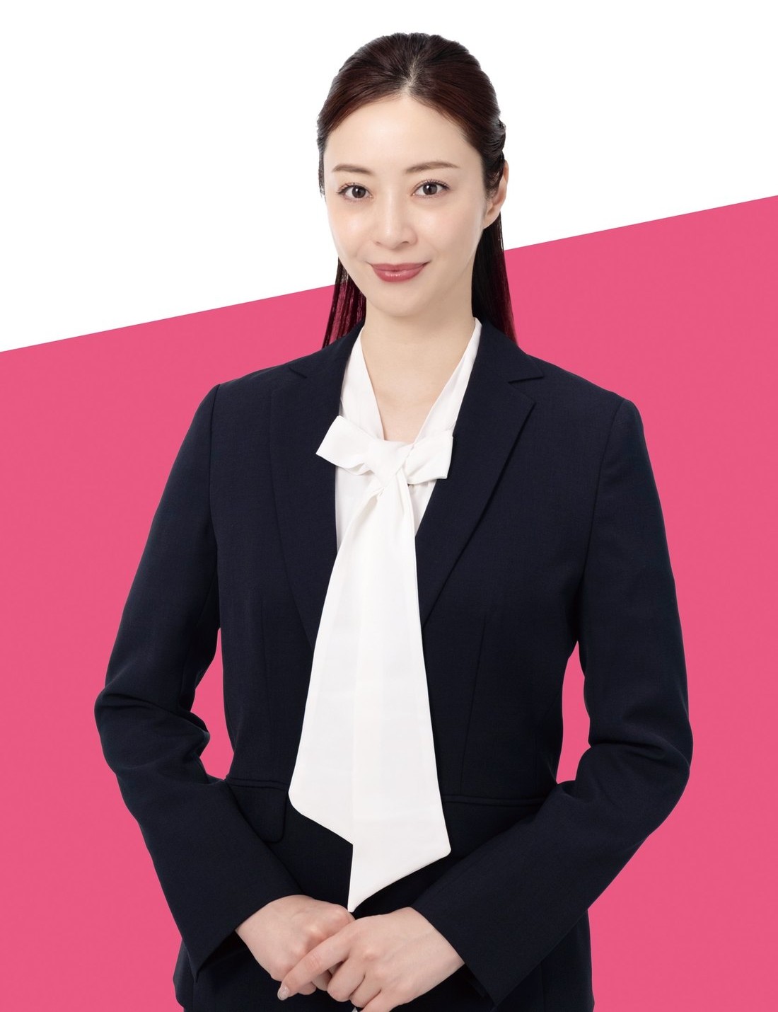 ピンクの背景を背に、手を前で組んで立つ白田久子